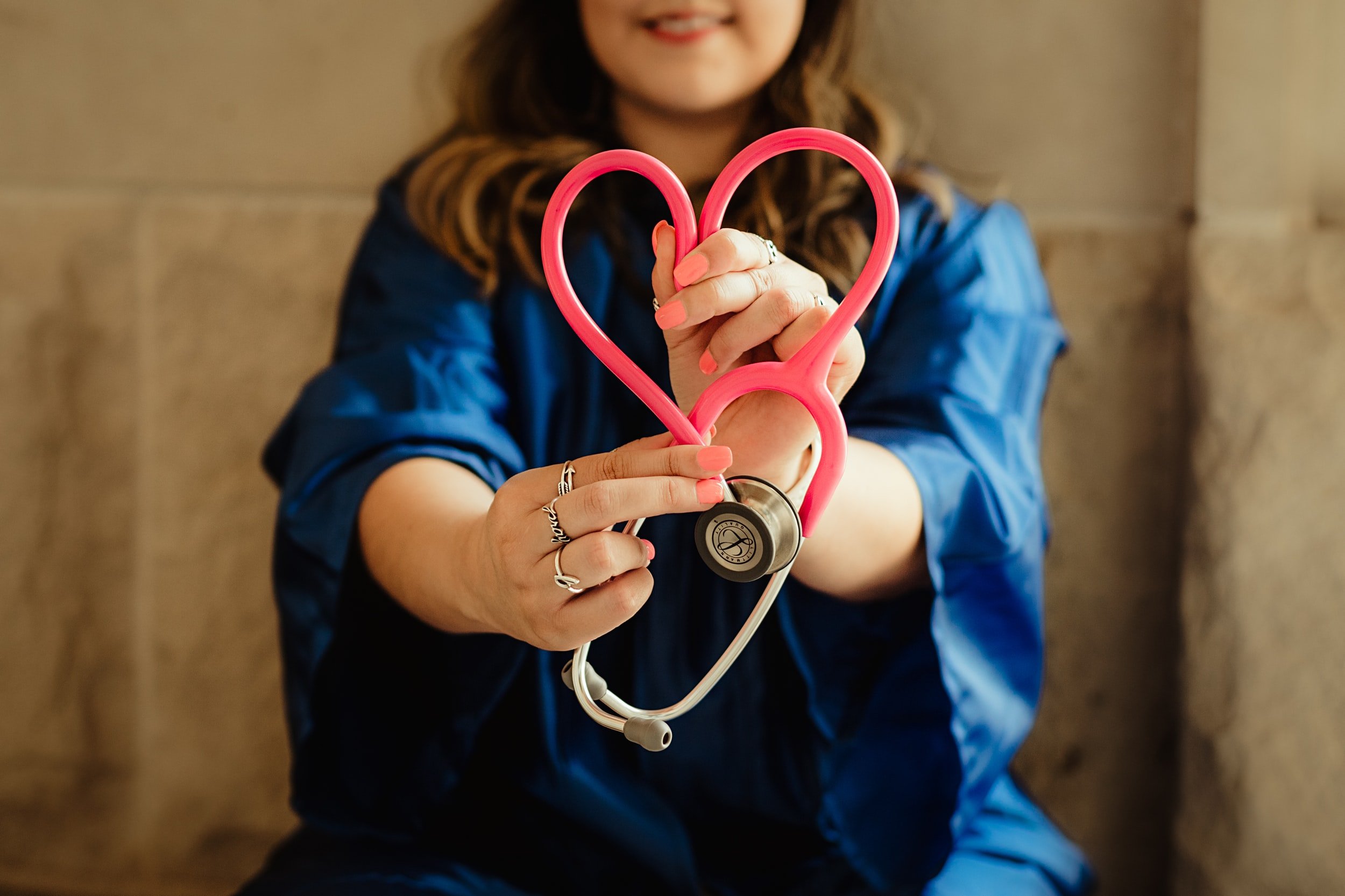 A nurse holding a pink stethoscope in the shape of a heart.